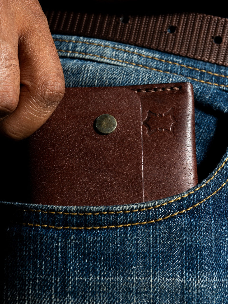 Brown leather  EDC wallet being placed into a blue denim pocket.
